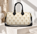 A structured satchel handbag with a cream-colored coated canvas body, covered in a repeating gold monogram pattern, featuring black leather top handles and a black shoulder strap with gold hardware.